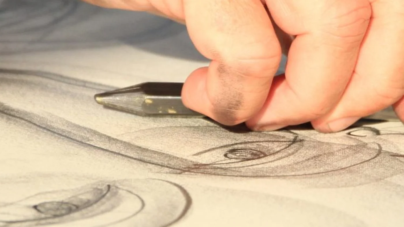 Gros plan d&rsquo;une main travaillant au crayon sur un grand dessin au fusain